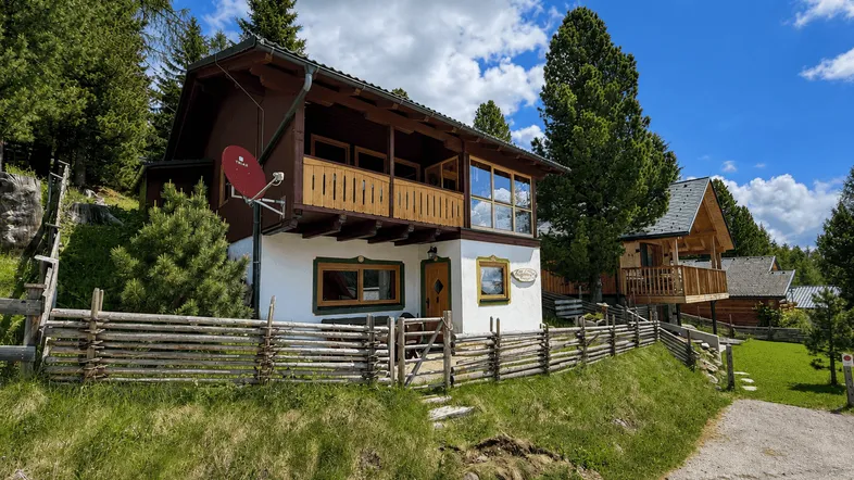 Traditionelles Alpenhaus mit Holzbalkon und Satteldach in bergiger Landschaft.