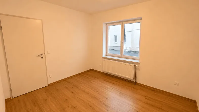 Helles Schlafzimmer mit Laminatboden, weißen Wänden und einem Fenster.