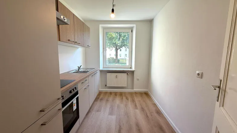 Schmale Küche mit hellen Holzoptikböden, modernen Einbauschränken und Fenster mit Blick ins Grüne.