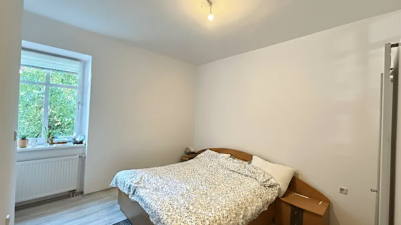 Helles Schlafzimmer mit Holzbett, Laminatboden und Fenster mit Blick ins Grüne.