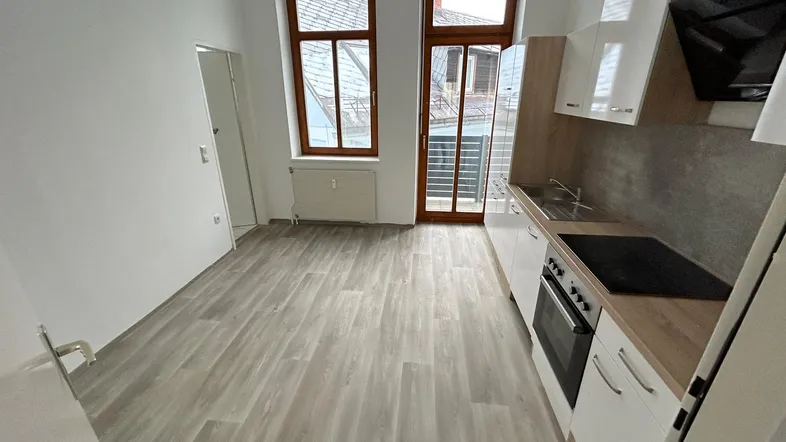 Helle Küche mit weißer Einbauküche, Holzoptik-Arbeitsplatte und Zugang zum Balkon.