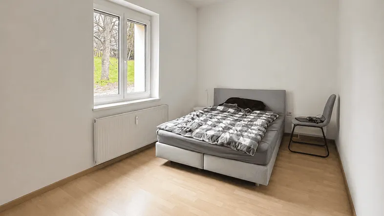 Helles Schlafzimmer mit Laminatboden, einem Doppelbett und Blick ins Grüne.