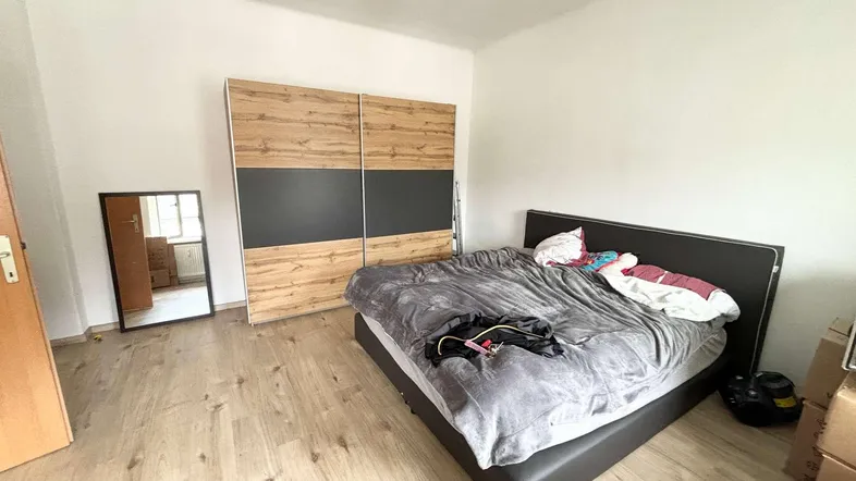 Helles Schlafzimmer mit Doppelbett, modernem Kleiderschrank und hellem Laminatboden, der den Raum freundlich wirken lässt.
