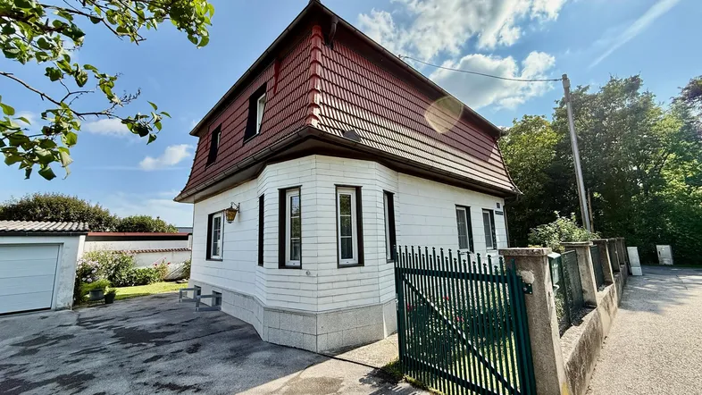 Traditionelles Einfamilienhaus mit Mansarddach, weißer Fassade und grünem Gartentor.