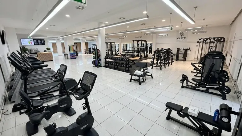 Modernes Fitnessstudio mit einer Vielzahl an Trainingsgeräten, hellen Fliesen und guter Beleuchtung.