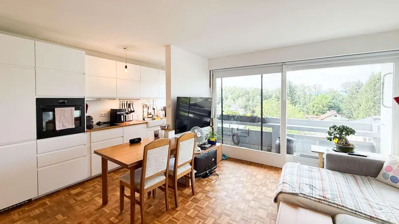 Heller offener Wohn-Essbereich mit integrierter Küche, Parkettboden und Zugang zum Balkon.