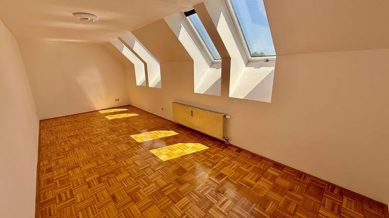 Helles Zimmer im Dachgeschoss mit Parkettboden und mehreren Dachfenstern, die viel Licht hereinlassen.