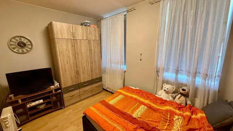 Helles Schlafzimmer mit Holzschrank, Doppelbett und Parkettboden, ausgestattet mit Vorhängen.