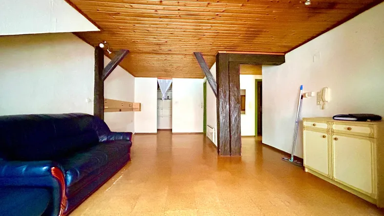 Gemütliches Wohnzimmer mit Holzbalkendecke, sichtbaren Holzpfosten und dunklem Ledersofa.