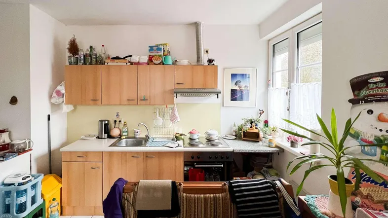 Helle Küche mit Holzschränken, Fliesenboden und einem Fenster, das Tageslicht hereinlässt.