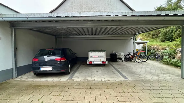 Geräumiger Carport mit Platz für ein Auto und Fahrräder, angrenzend an das Gebäude.
