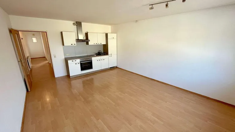 Heller offener Wohnbereich mit integrierter Küchenzeile und Laminatboden, ideal für modernes Wohnen.