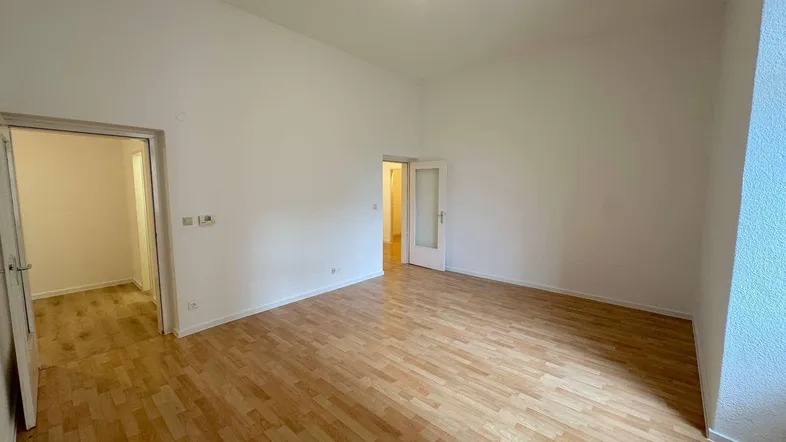 Helles, leeres Zimmer mit Laminatboden und Zugang zu weiteren Räumen.