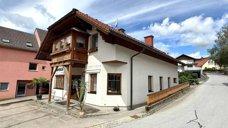 Traditionelles Gebäude mit Satteldach und Holzbalkonen in einer ländlichen Umgebung.