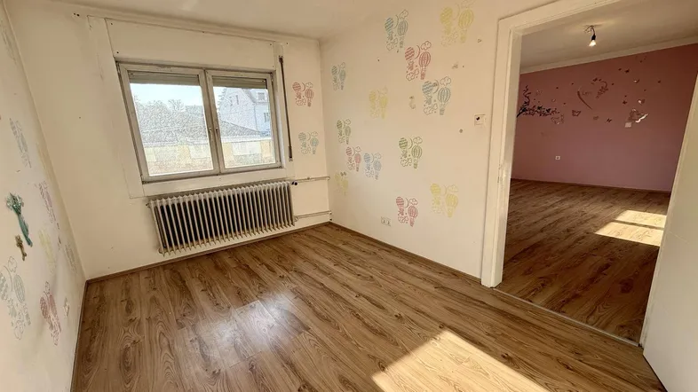 Helles Zimmer mit Laminatboden, bunten Wanddekorationen und Blick ins Nebenzimmer.