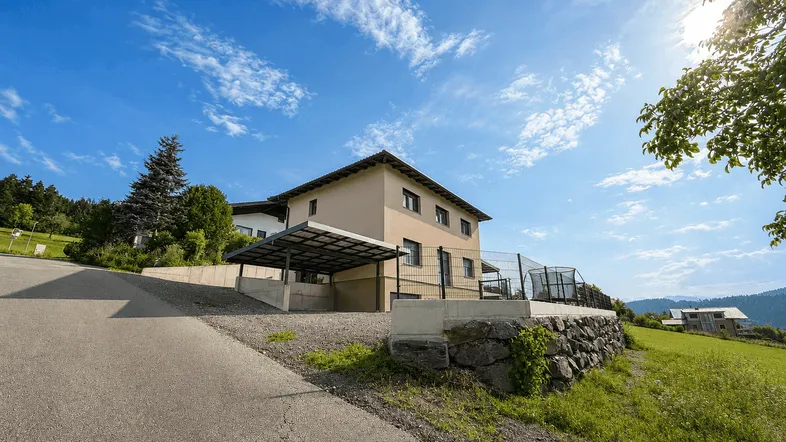Modernes Einfamilienhaus mit Carport und großem Garten in ländlicher Umgebung unter blauem Himmel.
