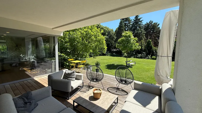 Große überdachte Terrasse mit modernen Loungemöbeln und Blick auf den gepflegten Garten.