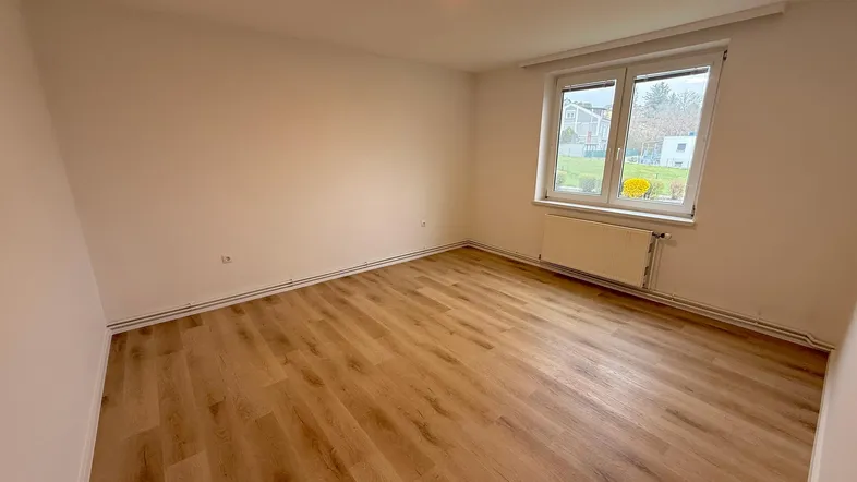 Helles Zimmer mit modernem Laminatboden und einem Fenster mit Blick ins Grüne.