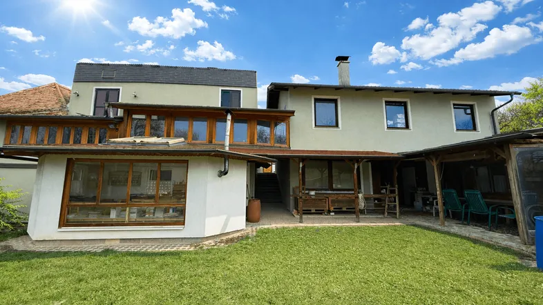 Großzügiger Gartenbereich hinter dem Haus mit Rasenfläche und Anbauten unter blauem Himmel.