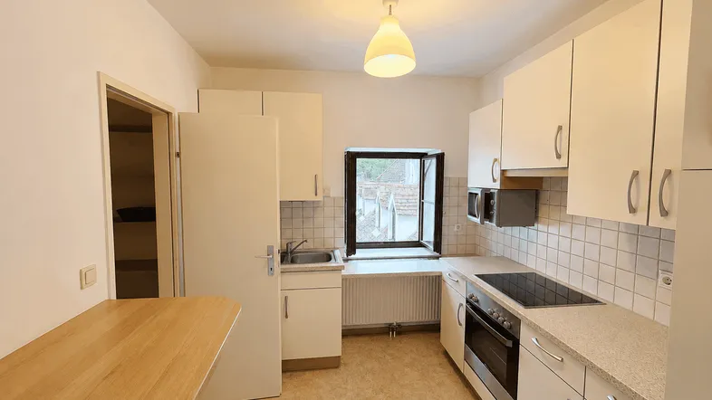 Helle Küche mit weißen Schränken, Fliesenrückwand und einem kleinen Fenster.