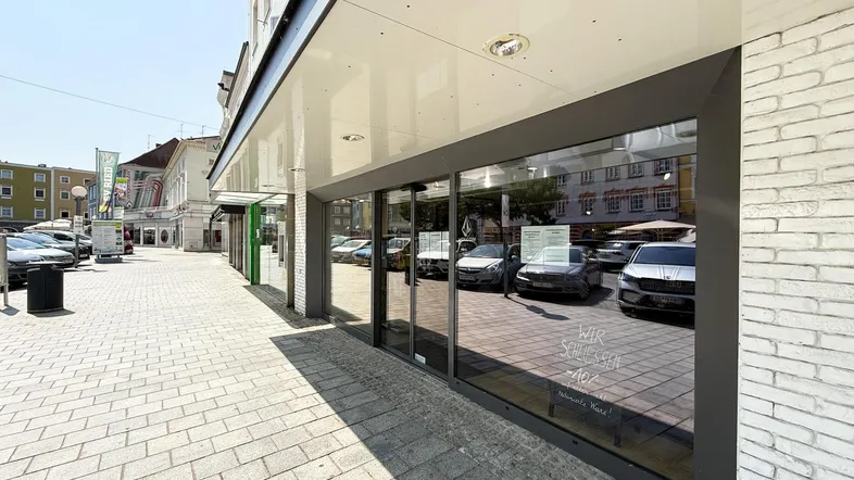 Nahaufnahme der Glasfront eines Geschäftsgebäudes mit reflektierenden Autos und einem Bürgersteig.