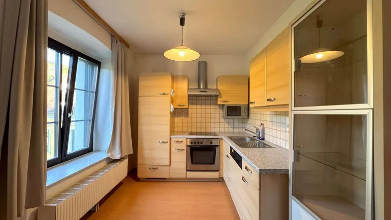 Helle Küche mit Holzfronten, Einbaugeräten und großem Fenster für natürliches Licht.