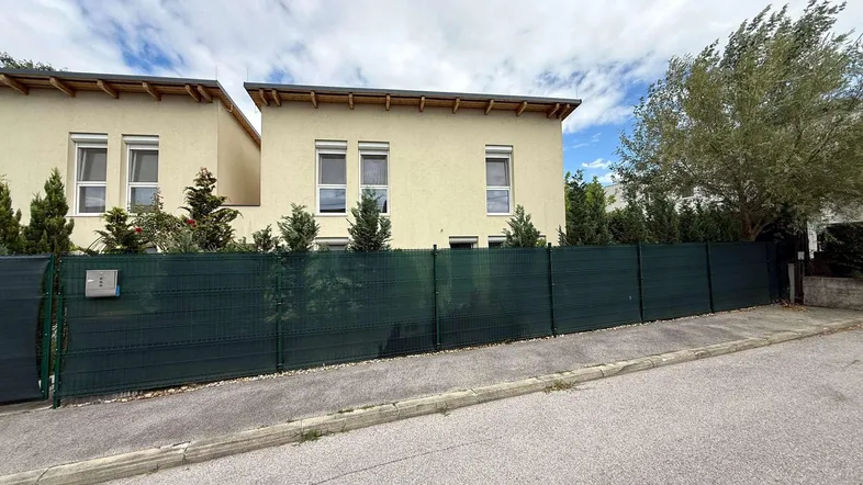 Zwei moderne Reihenhäuser mit heller Fassade und grüner Hecke entlang der Straße.