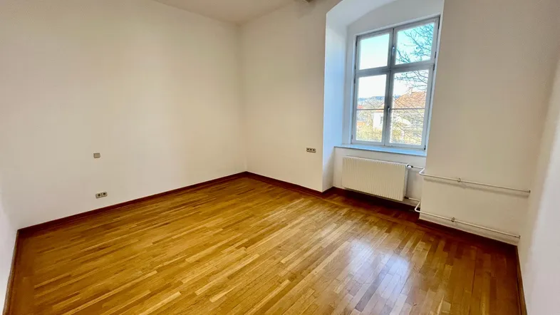 Helles, leeres Zimmer mit Holzboden und einem Fenster, das einen weiten Blick bietet.