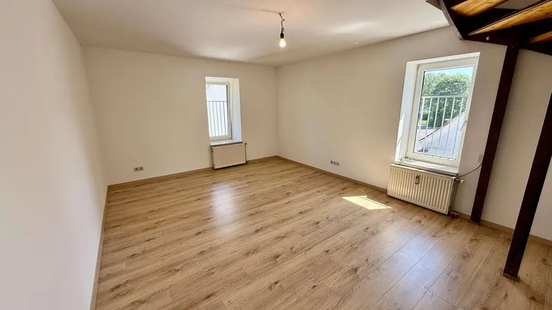Helles Zimmer mit Laminatboden, zwei Fenstern und Heizkörpern, ideal als Schlaf- oder Arbeitszimmer.