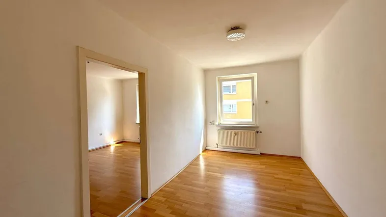 Geräumiger, heller Raum mit Parkettboden und Zugang zu einem weiteren Zimmer.