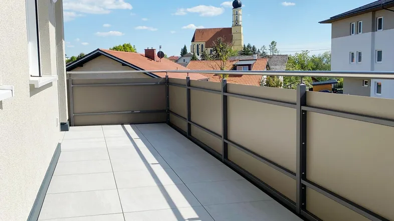 Heller Balkon mit Fliesenboden und Blick auf die Kirche unter blauem Himmel.