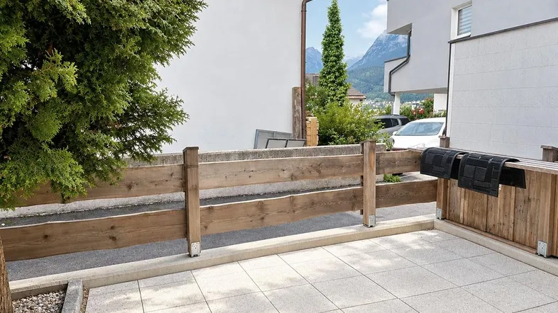 Gedeckte Terrasse mit Holzzaun und Blick auf die umliegende Berglandschaft und viel Grün.