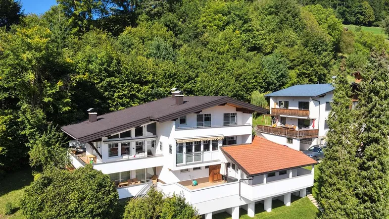 Großzügiges Wohnhaus in alpiner Umgebung, umgeben von üppiger Natur und Bäumen.