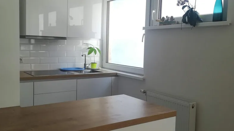 Helle Küche mit weißen Hochglanzschränken, Holztheke und Fenster für natürliches Licht.