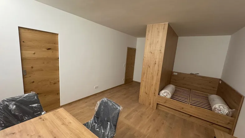 Heller Wohnbereich mit Holzboden, integriertem Schlafbereich und Esstisch in einem Neubau.