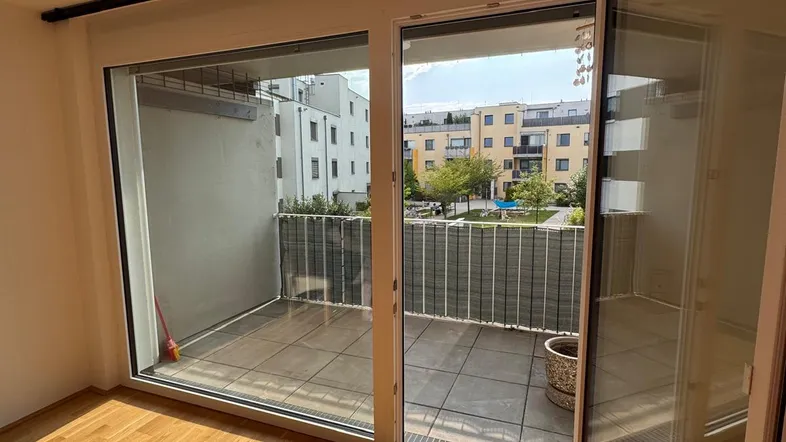 Heller Raum mit großen Schiebetüren, die auf einen gefliesten Balkon mit Blick ins Grüne führen.