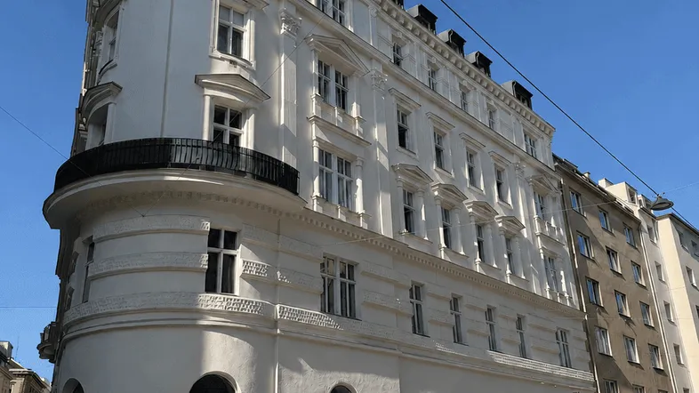Elegantes weißes Gebäude mit klassischer Architektur, vielen Fenstern und einem kleinen Balkon unter blauem Himmel.