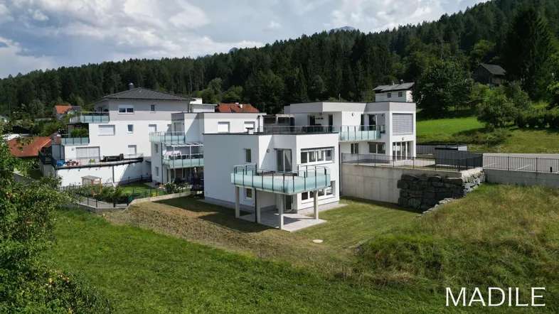 Luftaufnahme einer modernen Wohnanlage in grüner Hügellandschaft mit Blick auf die Umgebung und Berge.