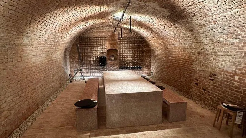Historischer Gewölbekeller mit freigelegten Ziegelwänden und modernem Verkostungstisch.