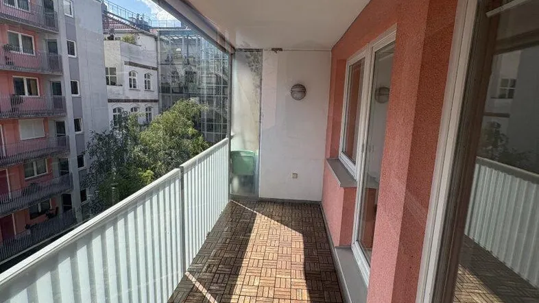 Sonniger Balkon mit Holzbodenfliesen und Glasbrüstung, ideal zum Entspannen im Freien mit Stadtblick.