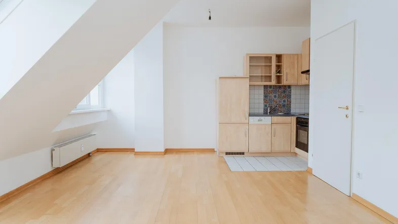 Helles Dachgeschosszimmer mit Holzboden und integrierter Küchenzeile unter der Dachschräge.