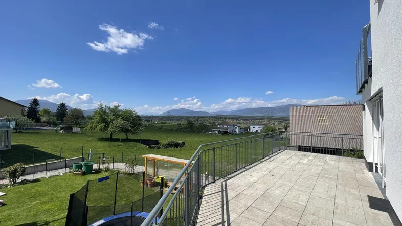 Große Terrasse mit Fliesenboden, weitem Blick ins Grüne und auf die Berge, mit Trampolin im Garten.
