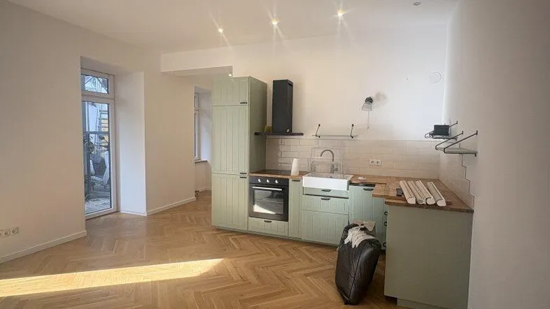 Funktionale Küchenzeile in hellem Grün mit integriertem Backofen und Spülbecken, Teil eines offenen Wohnbereichs.