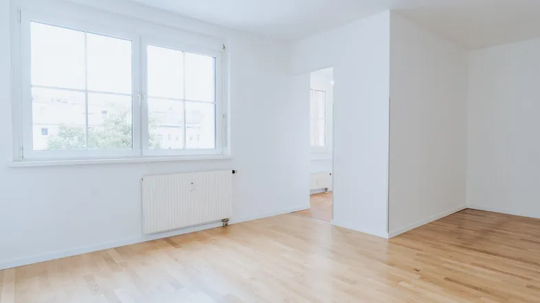 Helles, leeres Zimmer mit Parkettboden und großen Fenstern, bereit zur individuellen Gestaltung.