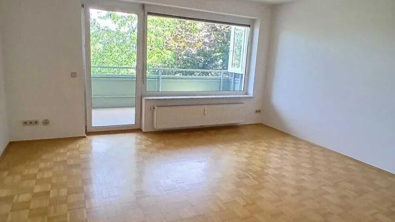 Helles, leeres Wohnzimmer mit Parkettboden und Zugang zu einem Balkon, ideal für individuelle Gestaltung.