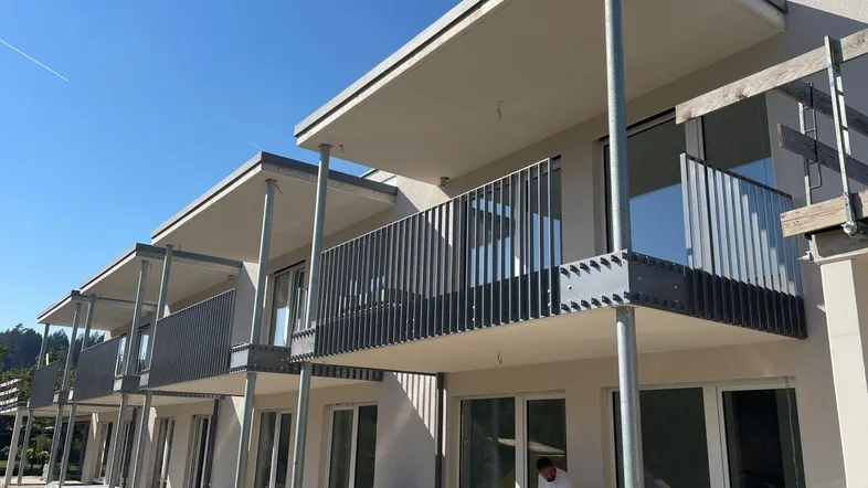Neubau mit mehreren modernen Balkonen und großen Fenstern unter strahlend blauem Himmel.