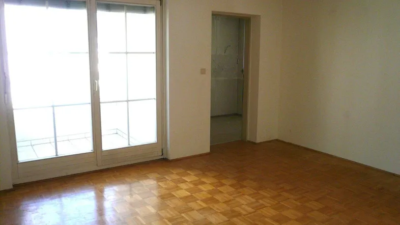 Helles Zimmer mit Parkettboden und Zugang zu einem Balkon, ideal als Wohn- oder Schlafbereich.
