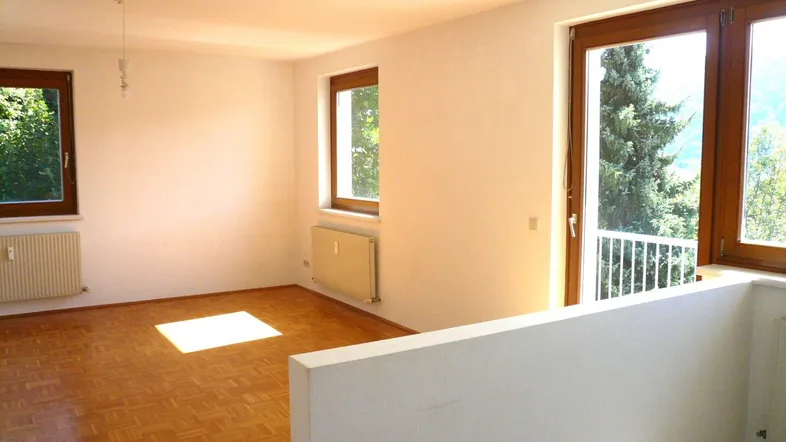 Helles, unmöbliertes Wohnzimmer mit Parkettboden und Zugang zu einem kleinen Balkon.