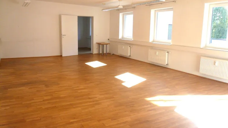 Geräumiger Büroraum mit hellem Parkettboden, großen Fenstern und viel Tageslicht.