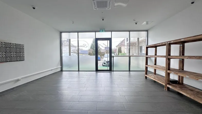 Geräumiger Gewerberaum mit großen Schaufenstern, Fliesenboden und Klimaanlage an der Decke.